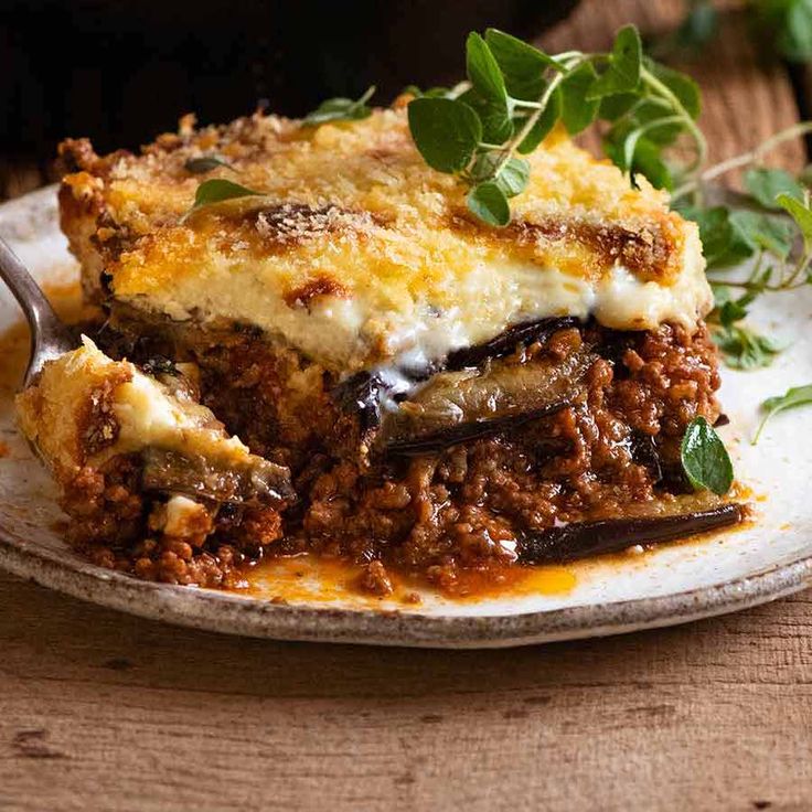 a white plate topped with lasagna covered in cheese and sauce on top of a wooden table