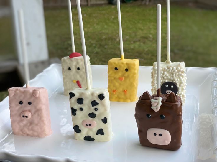 four marshmallows decorated like farm animals on a white platter with toothpicks