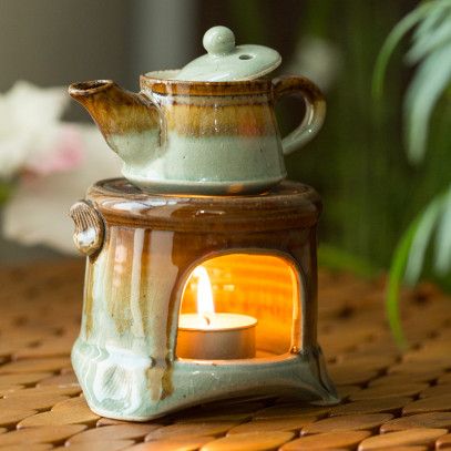 a tea pot with a lit candle in it sitting on a table next to a plant