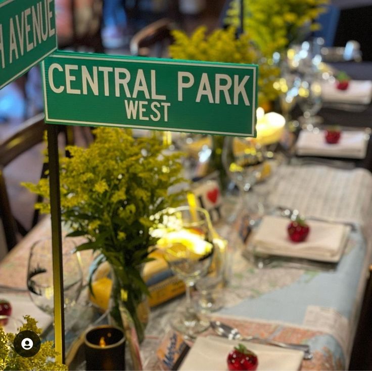 there is a green street sign that says central park west next to a long table with place settings