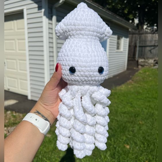 a crocheted stuffed animal is being held by someone's hand in front of a house