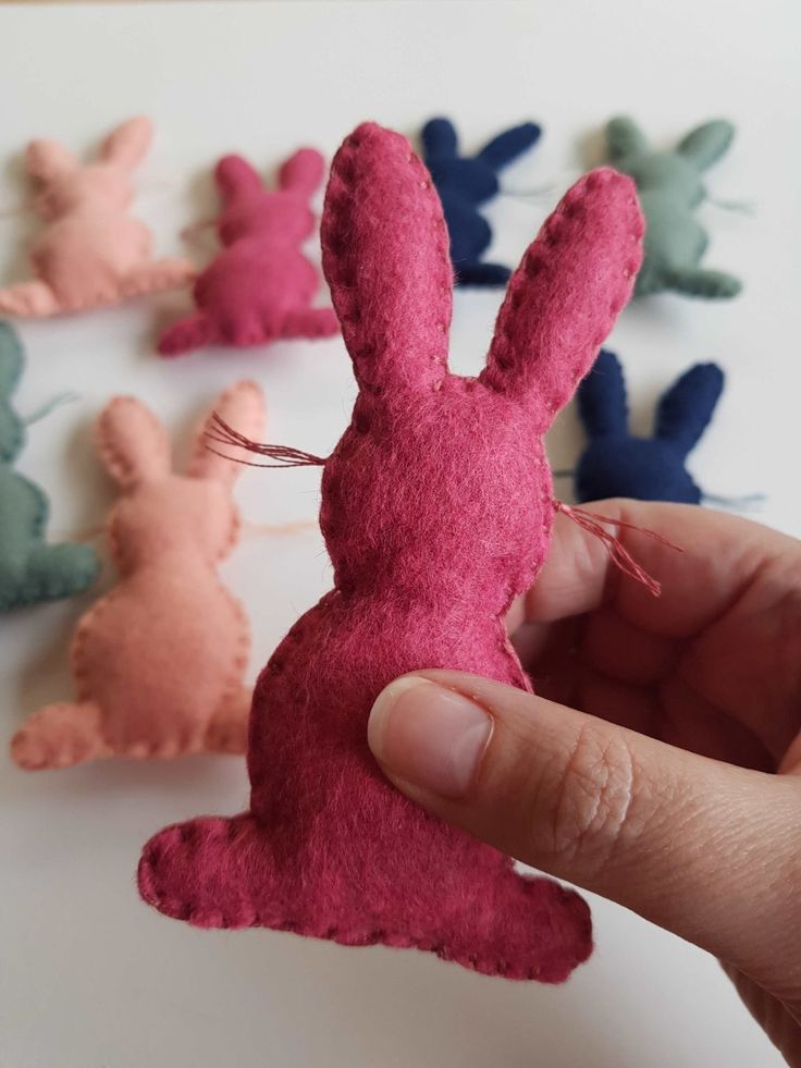 a hand holding a small felt bunny in front of several smaller ones on a table