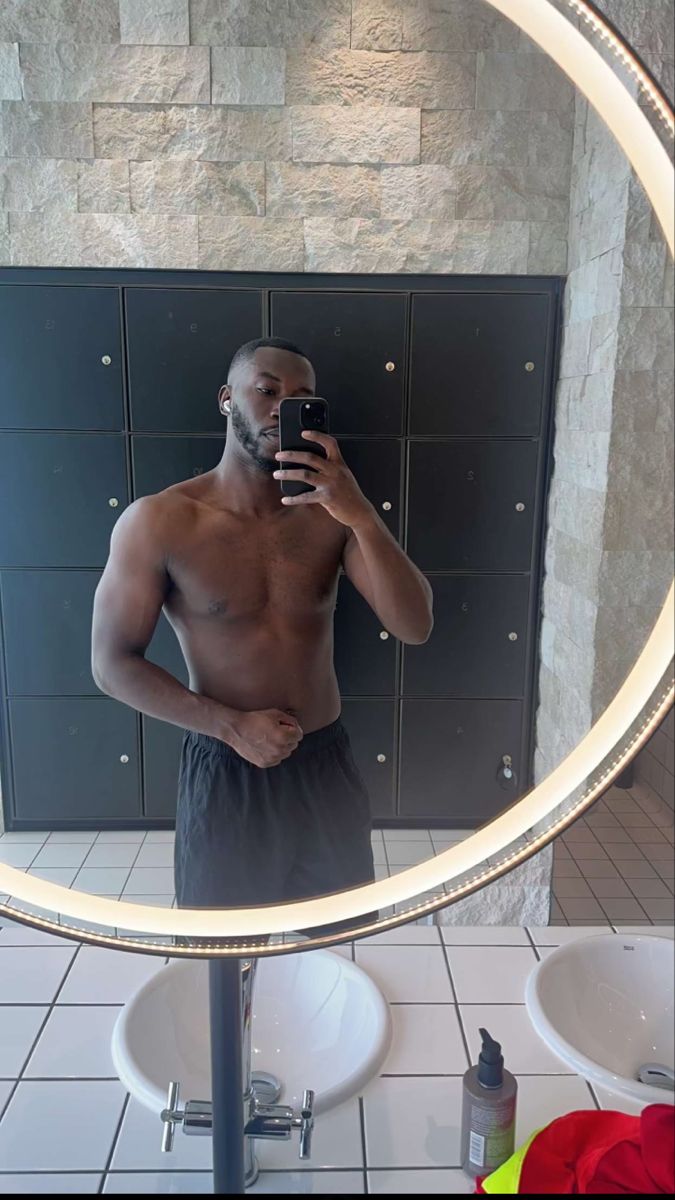 a shirtless man taking a selfie in front of a mirror with his cell phone