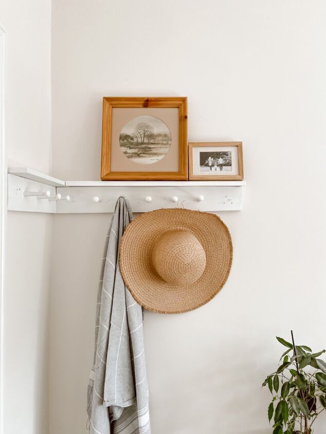 a hat is hanging on the wall next to a towel rack with two pictures and a potted plant