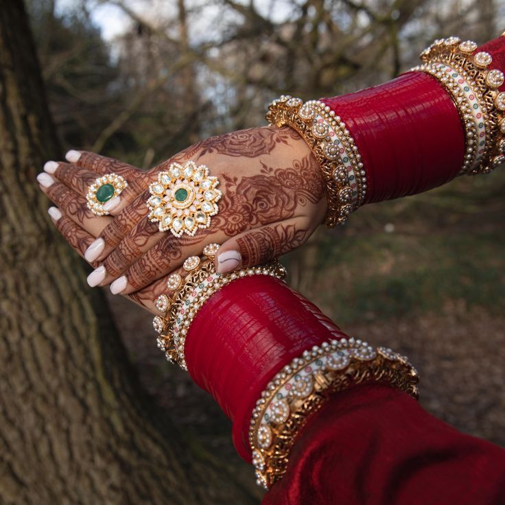 a woman's hands with henna and bracelets on her wrist, in front of a tree