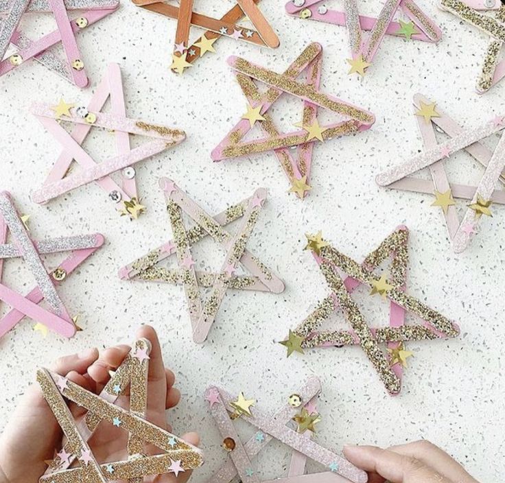 two hands are reaching for pink and gold stars on a white surface with glittery confetti