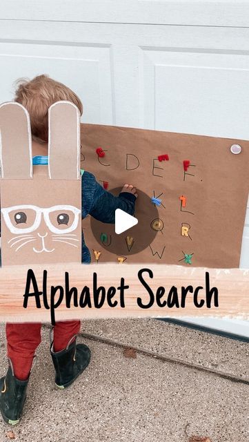 a young boy holding up a cardboard bunny with the words alphabet search in front of him