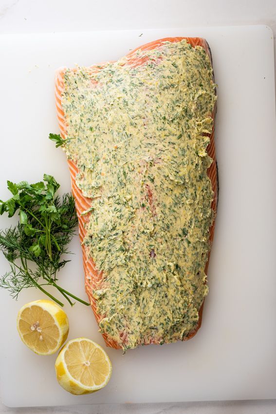 a piece of salmon on a cutting board with lemons and parsley next to it