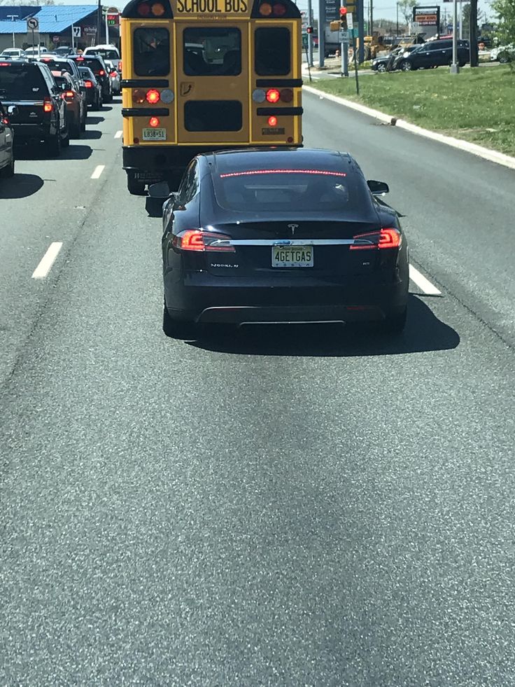 a school bus driving down the road with cars behind it and a black sports car in front