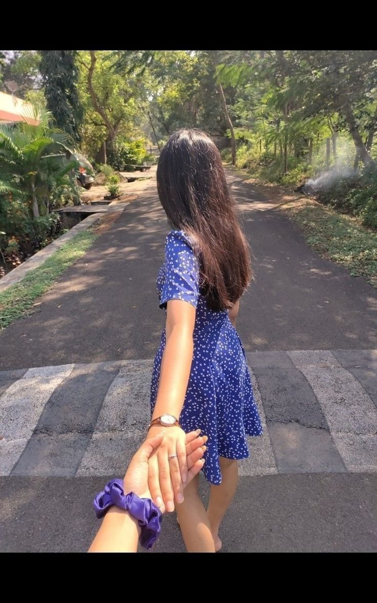 two people holding hands while walking down the street in front of some trees and bushes