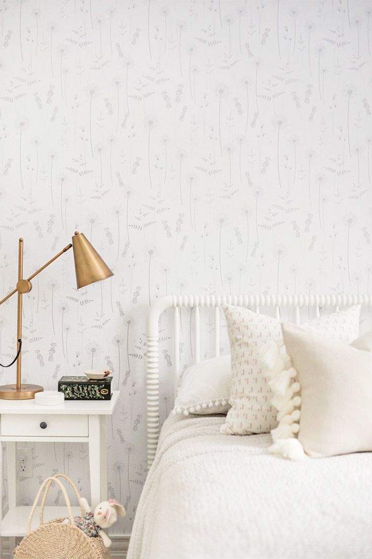 a white bed sitting under a lamp next to a table with a basket on it