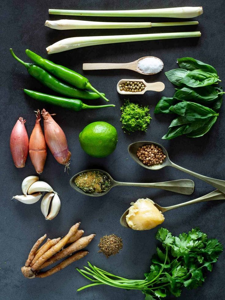 an assortment of vegetables are arranged on a black surface with spoons and measuring spoons