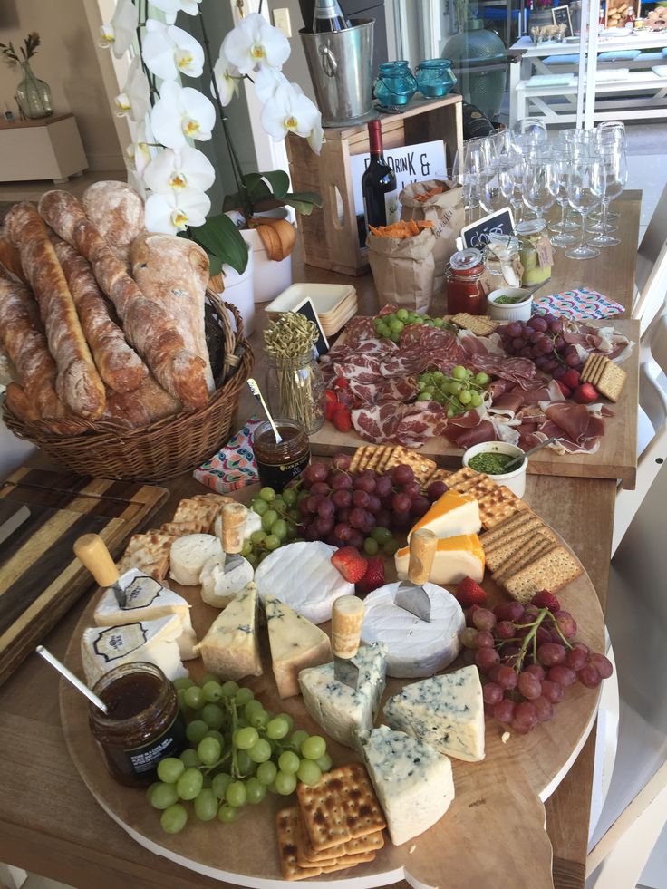 a wooden table topped with lots of cheeses and crackers next to wine glasses