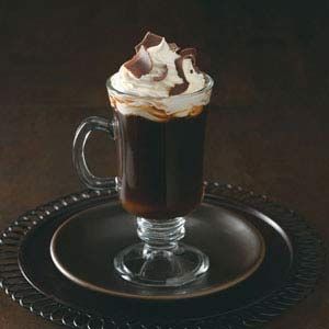 a glass cup filled with hot chocolate and whipped cream on top of a black plate