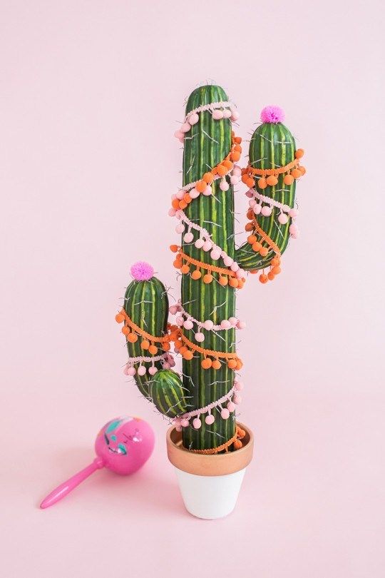 a cactus with decorations around it on a pink background next to a potted plant