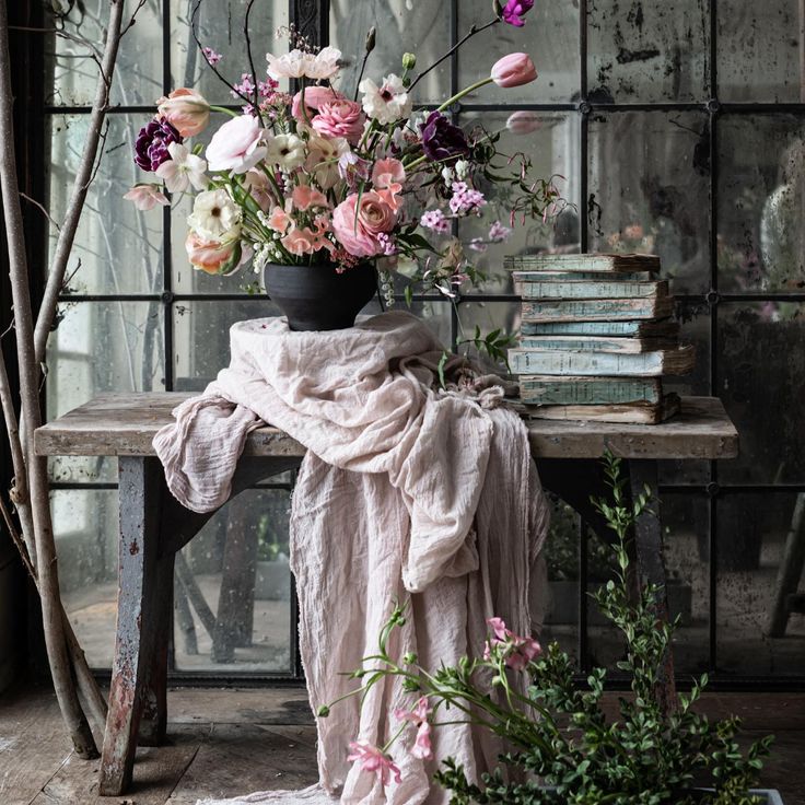 an arrangement of flowers in a vase sitting on a table next to a stack of books