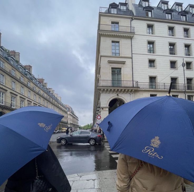 two people walking down the street with umbrellas in front of their heads and cars behind them