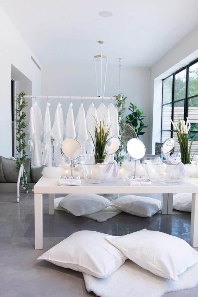 a white table topped with lots of pillows next to a mirror and plant in vases