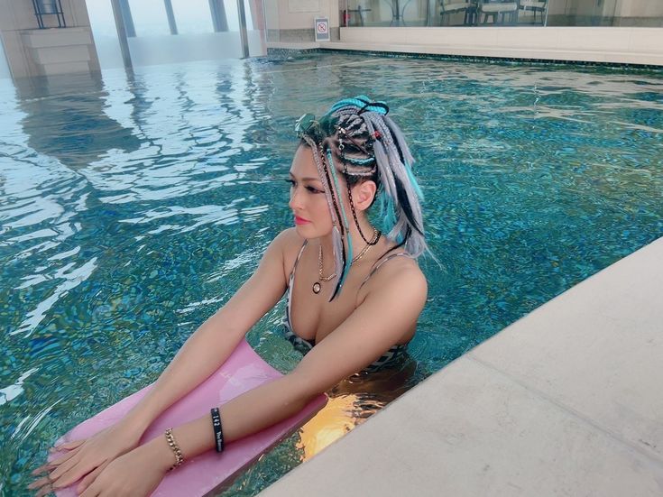 a woman sitting on a pink surfboard in a swimming pool with her hair pulled back