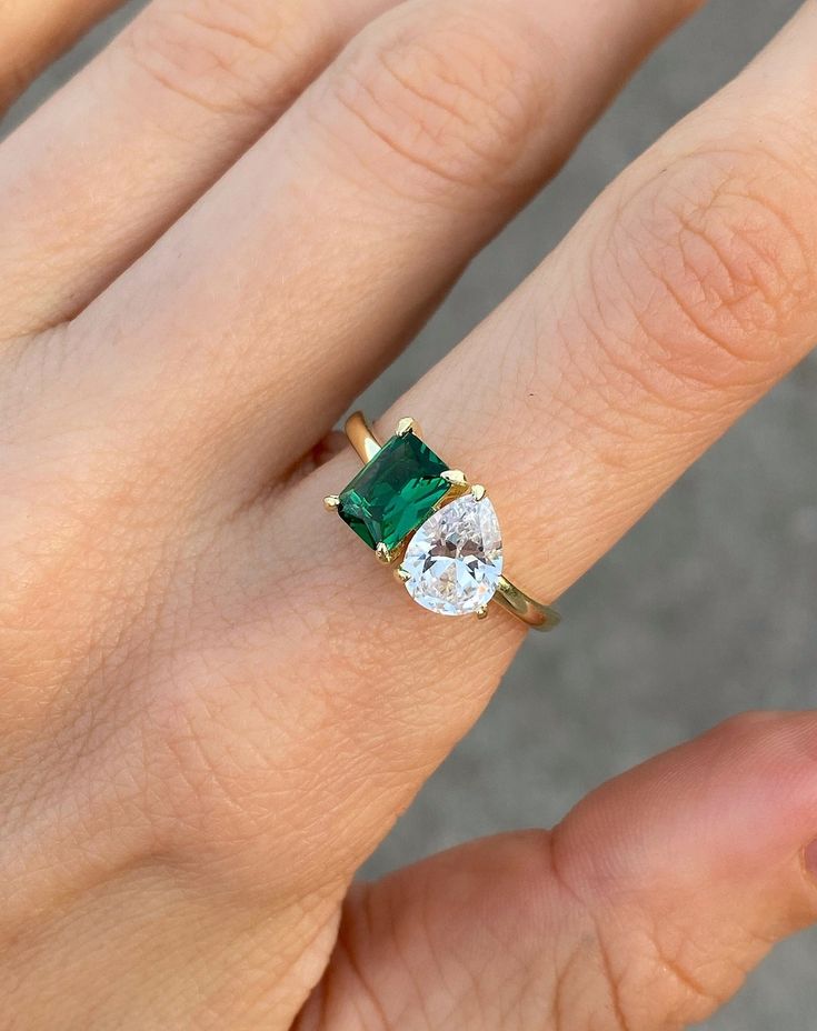 a woman's hand holding a ring with an emerald and white diamond on it