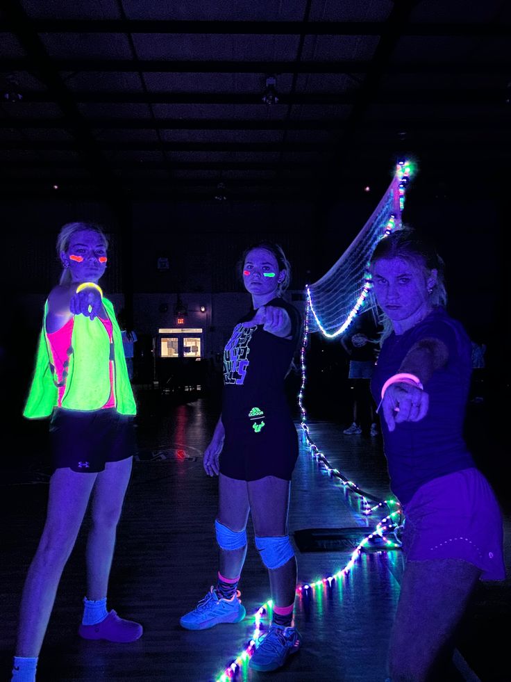 three girls are standing in the dark with their arms around each other and lights on