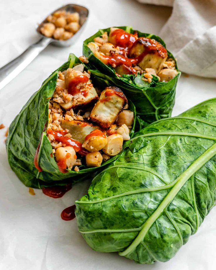 two lettuce wraps filled with meat and vegetables on top of a white surface