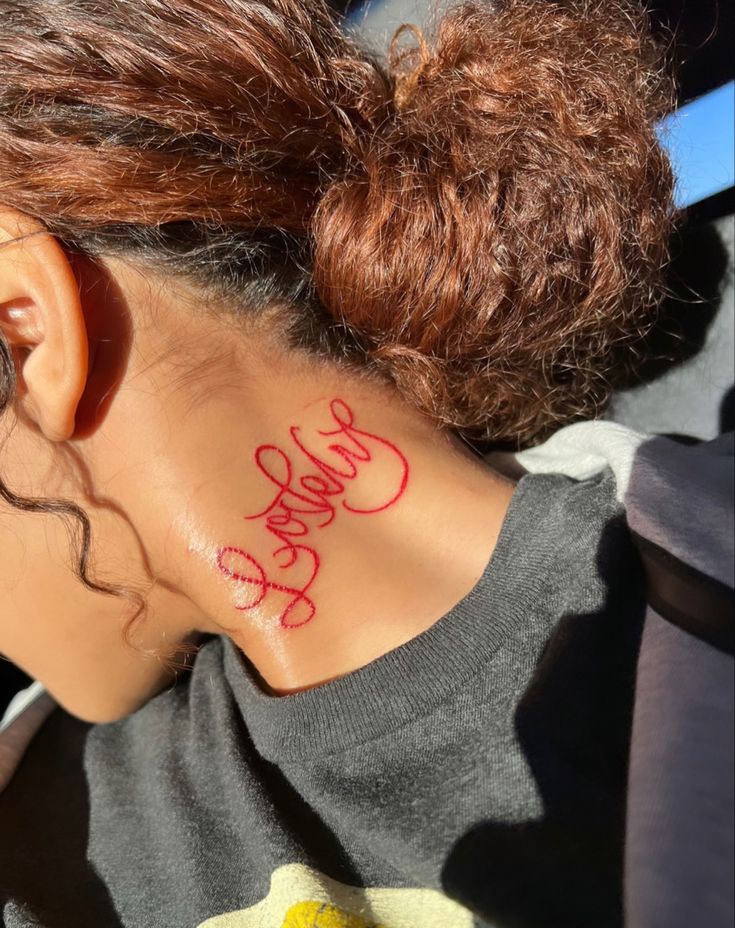 the back of a woman's neck with red writing on her left shoulder and behind her ear