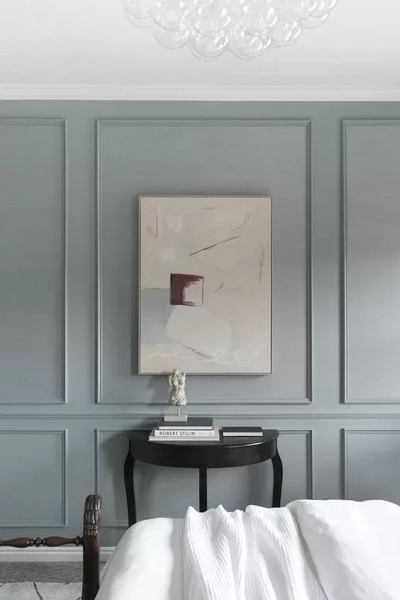 a white bed sitting under a painting on the wall next to a table and chair