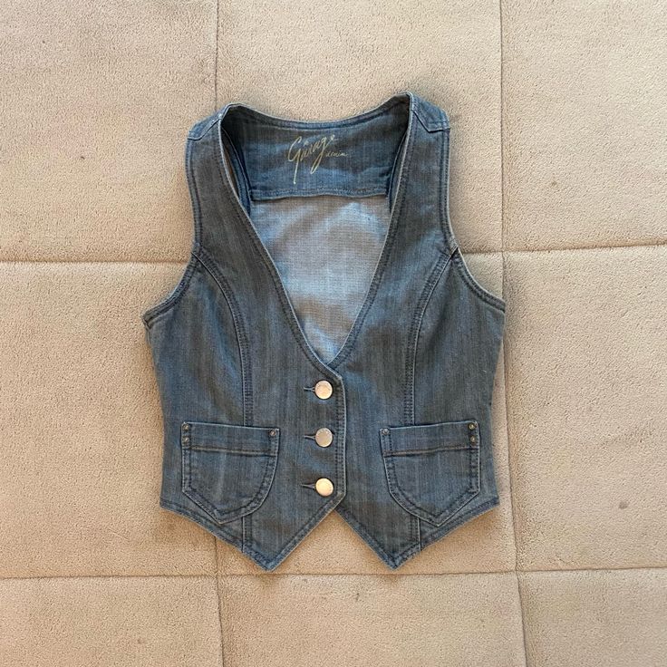 a blue jean vest with buttons on the front and back, sitting on a beige surface