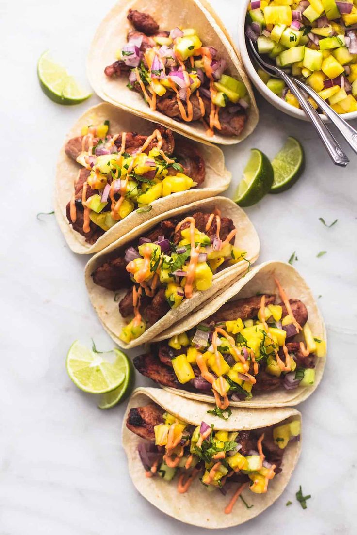 four tacos with meat, pineapple salsa and avocado on them next to a bowl of limeade