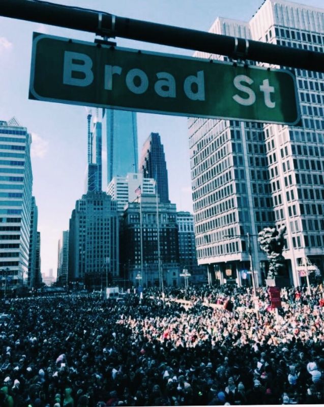 a street sign that reads broad st in front of a large group of people and skyscrapers