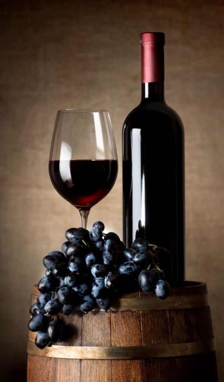 a wine glass and bottle sitting on top of a wooden barrel next to some grapes