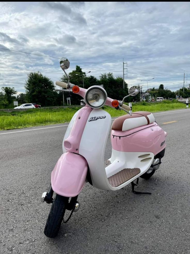 a pink and white scooter is parked on the side of the road with grass in the background