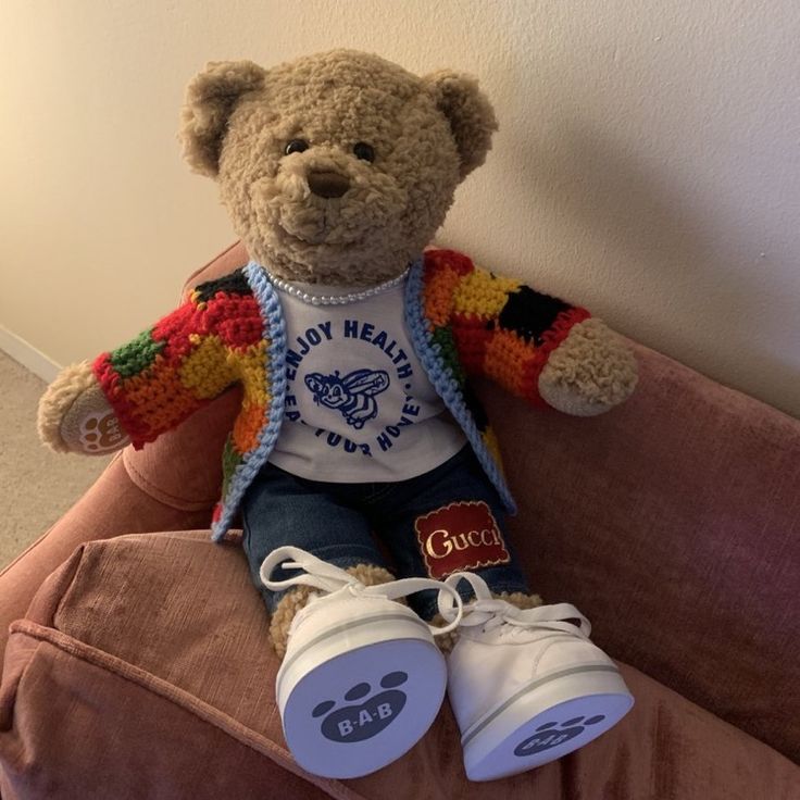 a teddy bear sitting on top of a couch wearing a shirt and jeans with white sneakers