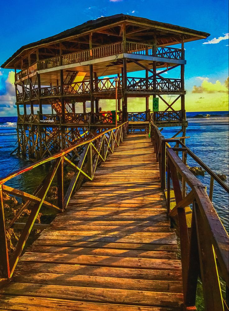 a wooden dock leading into the ocean with a life guard tower in the background at sunset