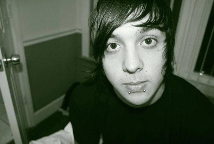 a young man with piercings on his nose looking at the camera while sitting in front of a mirror