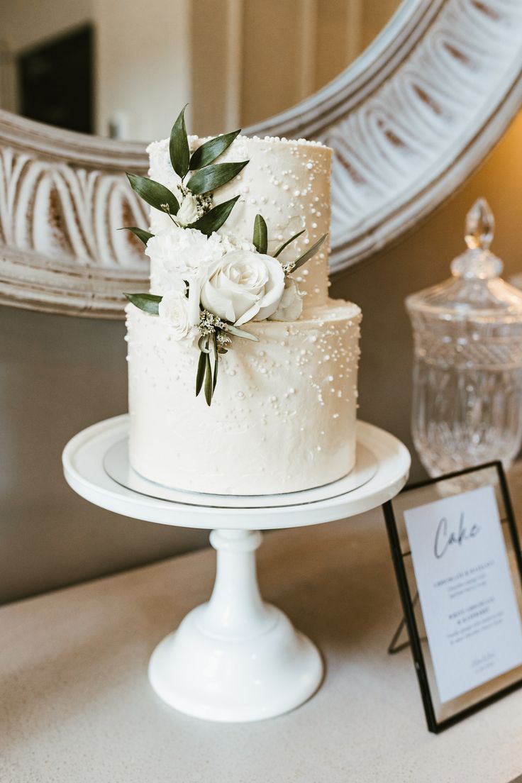 a white wedding cake sitting on top of a table next to a framed photo and mirror