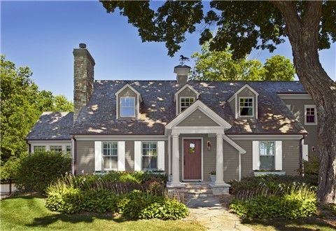 a gray house with white trim and two story windows on the front, surrounded by greenery