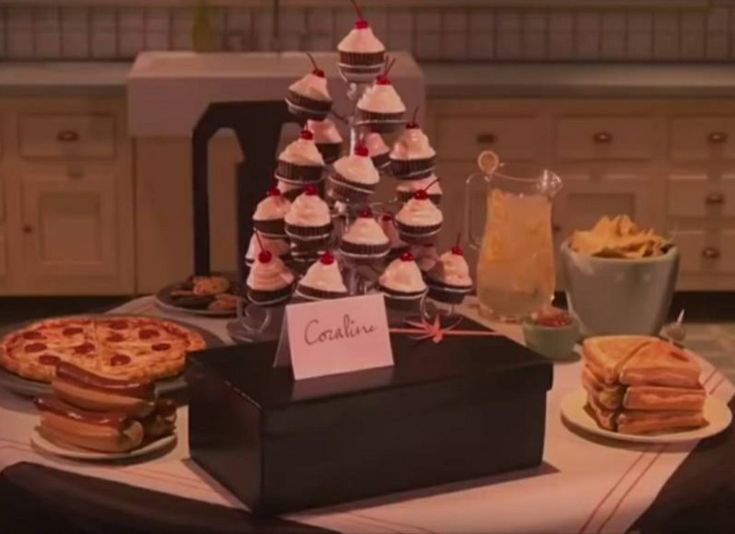 a table topped with cakes and cupcakes next to a woman looking at it