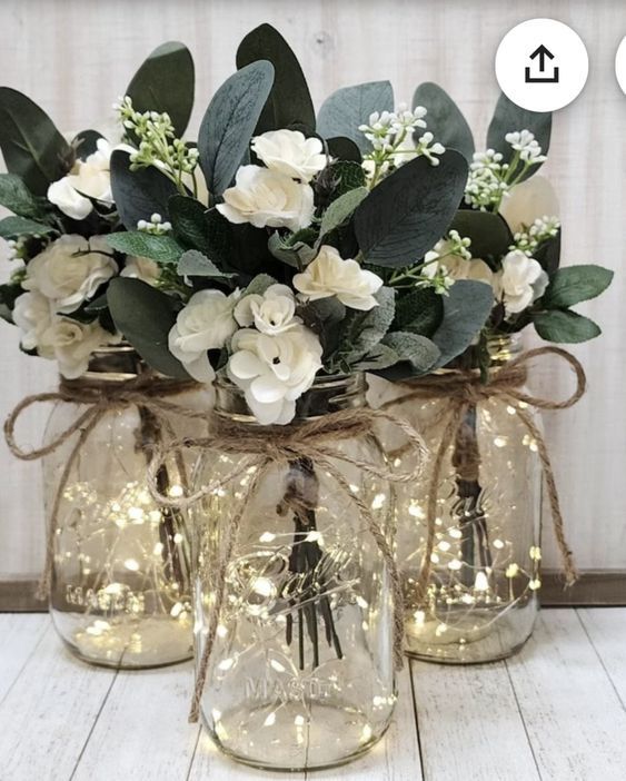 three mason jar vases with flowers and lights on the inside one is filled with greenery