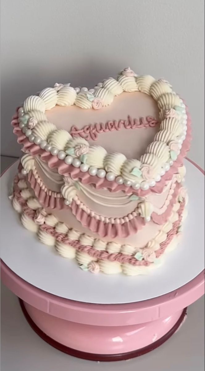 a heart shaped cake on top of a pink stand with white frosting and seashells