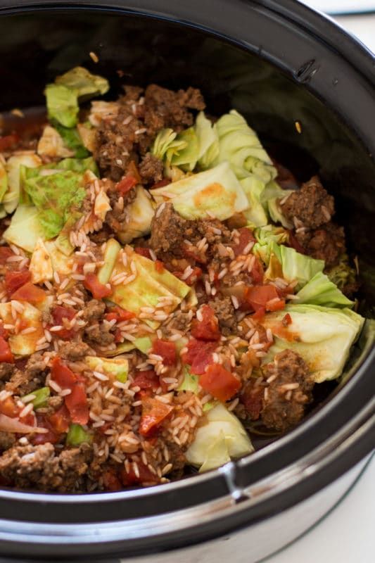 a slow cooker filled with meat, lettuce and tomato slices on top