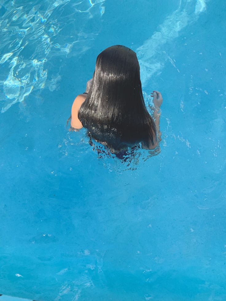 a woman with long black hair swimming in a pool