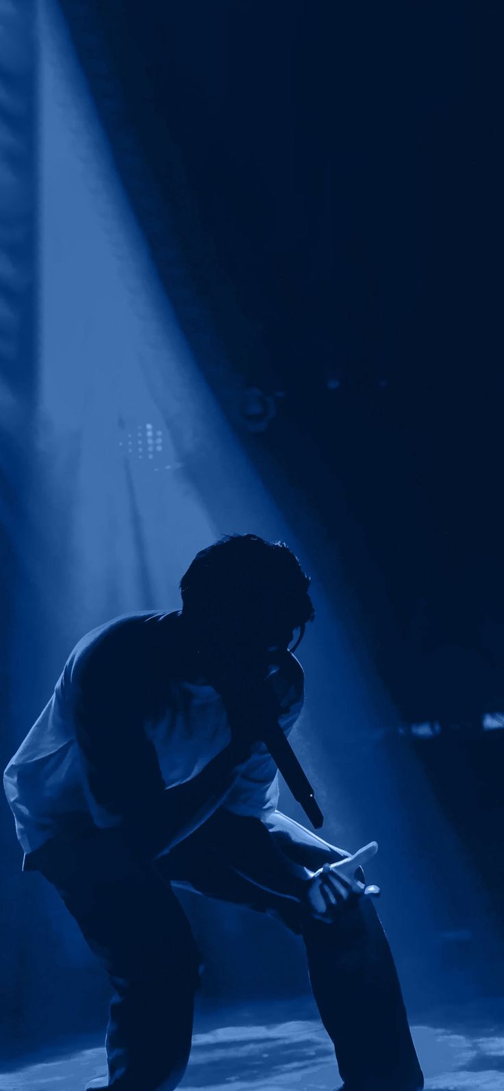 a man kneeling down on top of a stage with a microphone in his hand and lights behind him