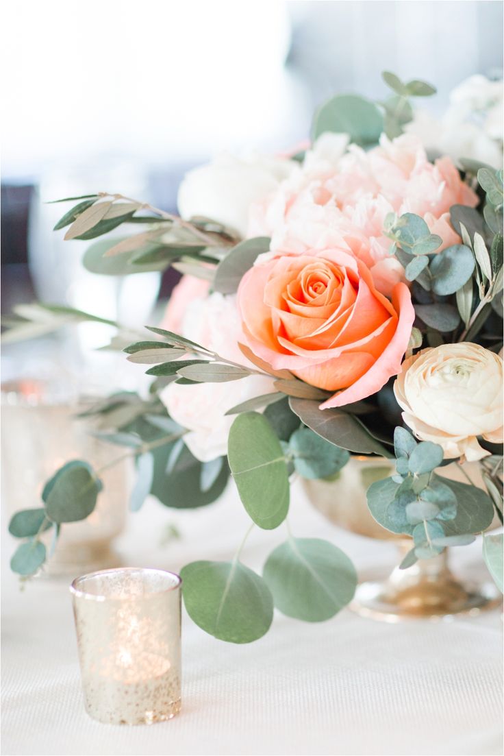 a vase filled with flowers and greenery on top of a table next to a candle