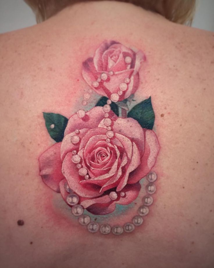 a woman's back with a pink rose and pearls tattoo on her left shoulder