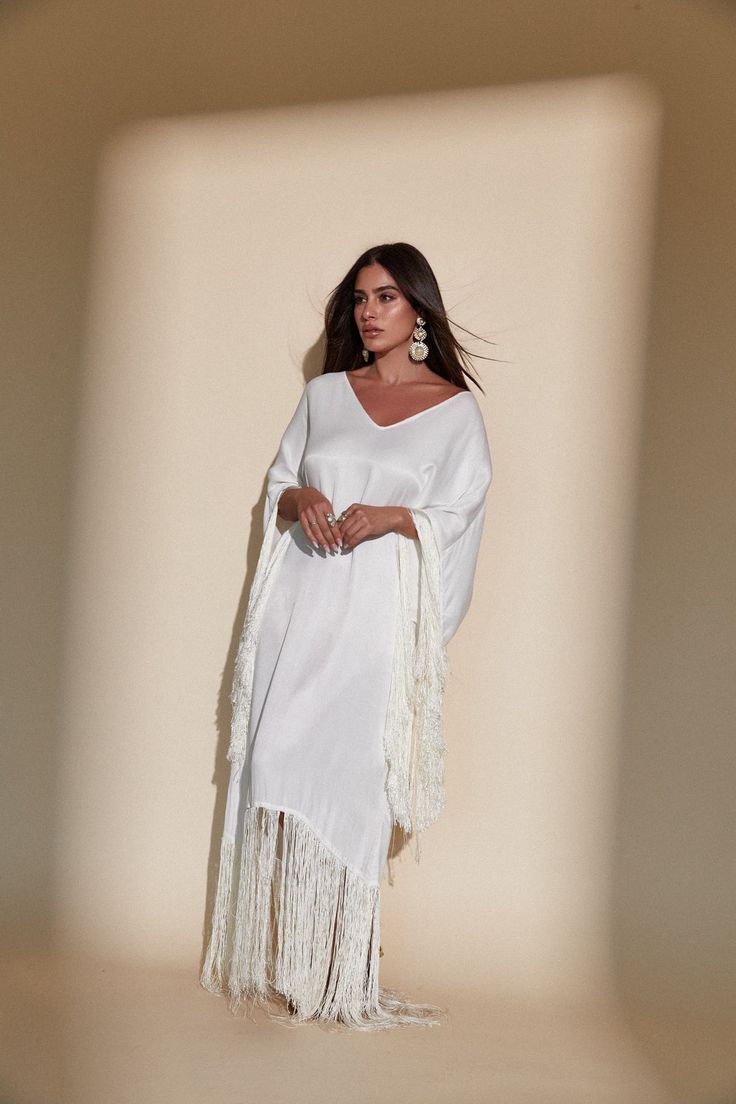 SOL FRINGE KAFTAN - OFF WHITE – Kadimah Vacation V-neck Kaftan With Tassel Ties, Elegant White V-neck Kaftan, Spring Kaftan With Tassels And Kimono Sleeves, White Maxi Dress With Tassels, White Fringe V-neck Dress, White V-neck Dress With Fringe, Elegant Long Sleeve Kaftan With Tassels, Chic White Kaftan For Beach Cover-up, Spring Maxi Kaftan With Tassels