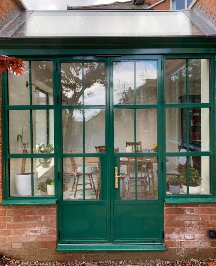 a house with green doors and windows on the outside, in front of a brick building