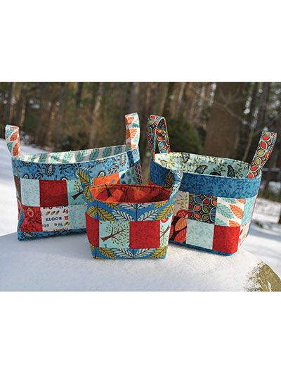 three quilted baskets sitting on top of snow covered ground with trees in the background