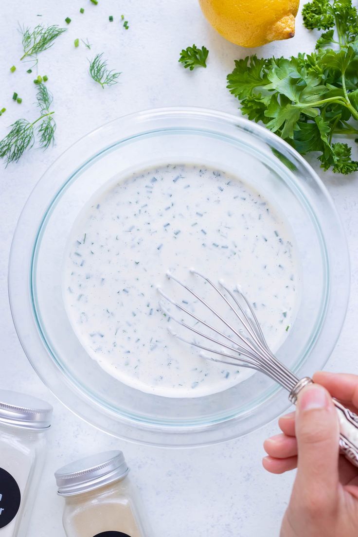 someone is whisking the dressing in a glass bowl next to lemons and parsley